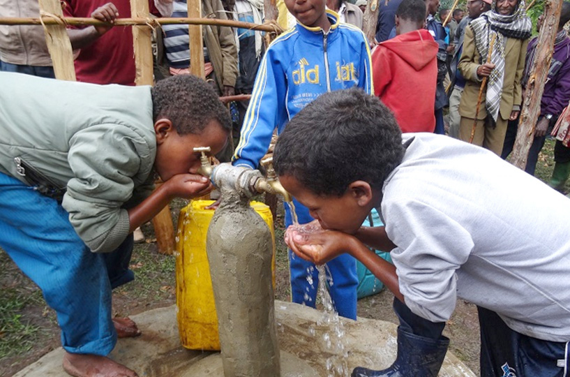 Kinder die vom Brunnen Wasser trinken