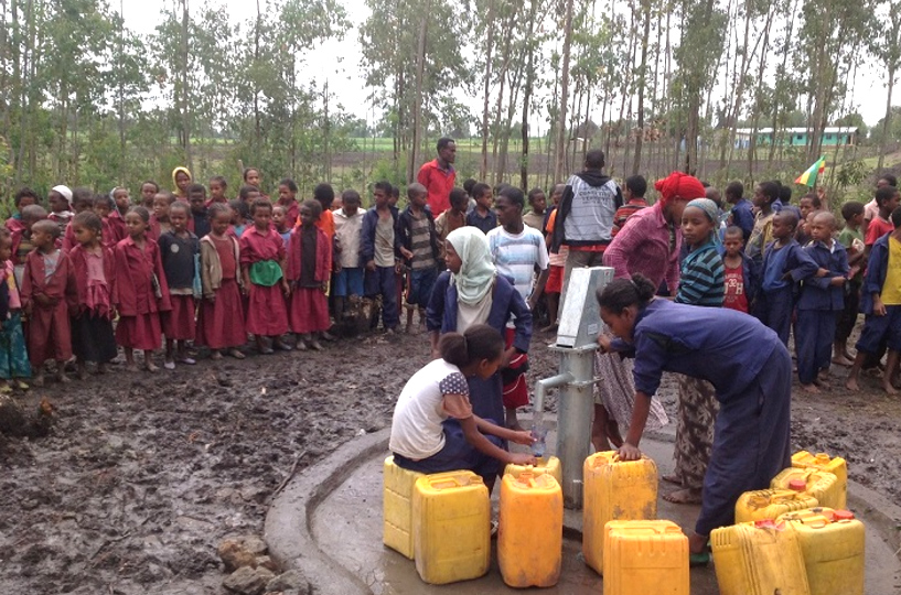Viele Kinder und Frauen mit Kanistern an einem Brunnen